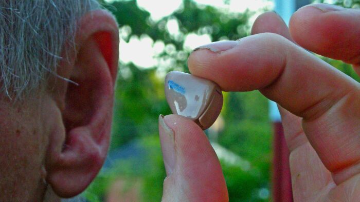 Close-up of a person holding a hearing aid near their ear, illustrating peer pressure and unwanted plastic surgery topics.
