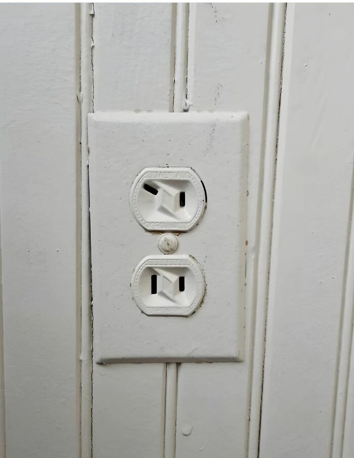 Old c*****d electrical outlet on a white wooden wall found in an abandoned or forgotten home.
