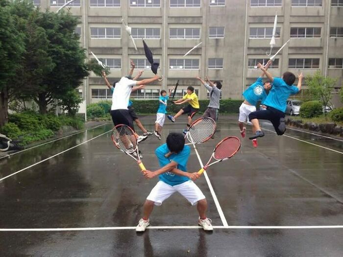 Group of people on a wet court striking creative poses with tennis rackets and mid-air jumps, showcasing hilarious and creative poses.