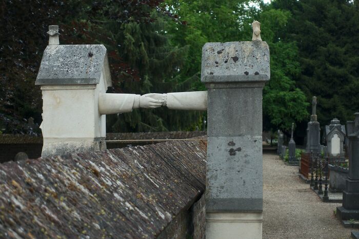 Stone sculptures of two arms reaching and holding hands above a cemetery wall, symbolizing crazy things people did for love.