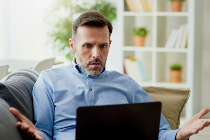 Man in blue shirt looking shocked while reading texts on laptop, hinting at husband suspected as psychopath mystery. Man in blue shirt looking shocked while reading texts on laptop, hinting at husband suspected as psychopath mystery.