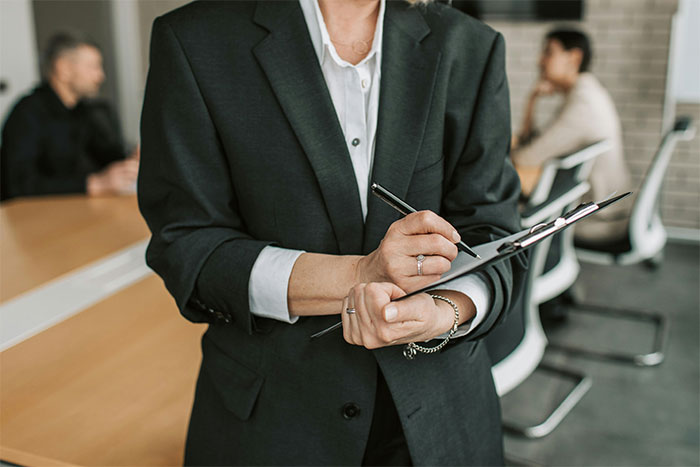 HR professional holding a clipboard and pen in a meeting room, addressing employee resistance to unpaid training duties. HR professional holding a clipboard and pen in a meeting room, addressing employee resistance to unpaid training duties.