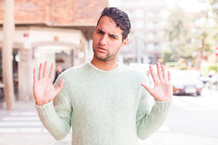 Man in a light green sweater with raised hands showing rejection, representing women shutting down men’s creepy advances.