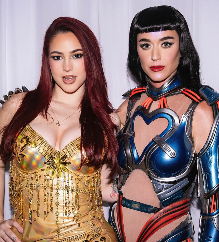 Two women posing together, one in gold outfit and the other in futuristic armor, related to Katy Perry's grim response controversy.