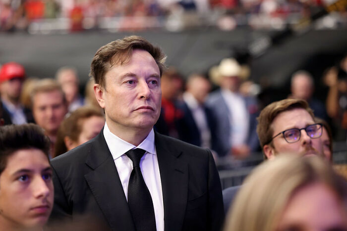 Man in black suit and tie attending a crowded event, representing shaky industries facing potential collapse risks.