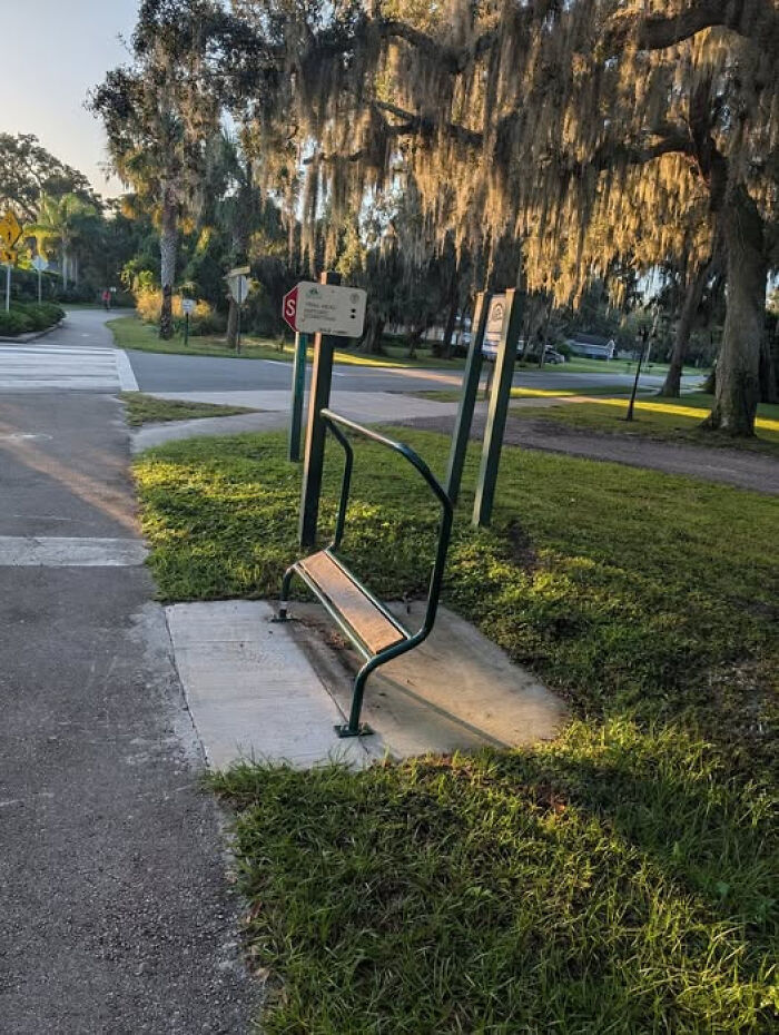Unidentified object resembling a partial bench in a park setting with trees and street signs in the background.