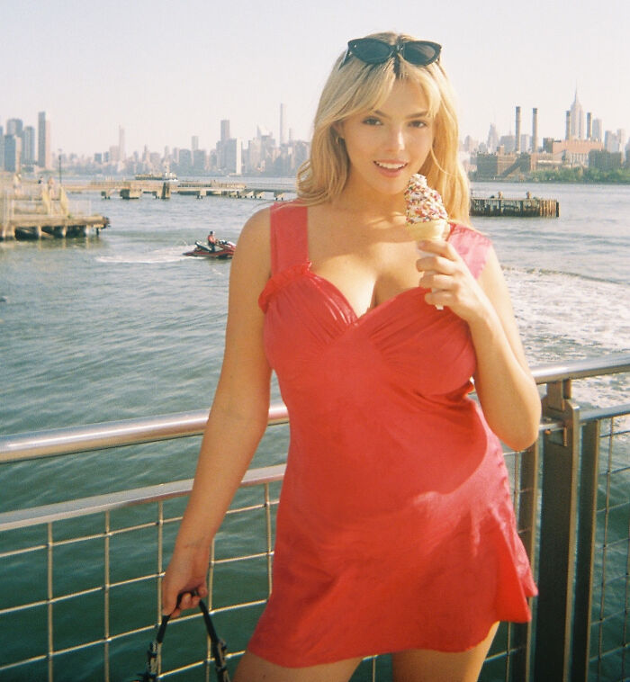 Woman in a red dress holding ice cream by the waterfront, related to David Harbour’s alleged partner incident at party.