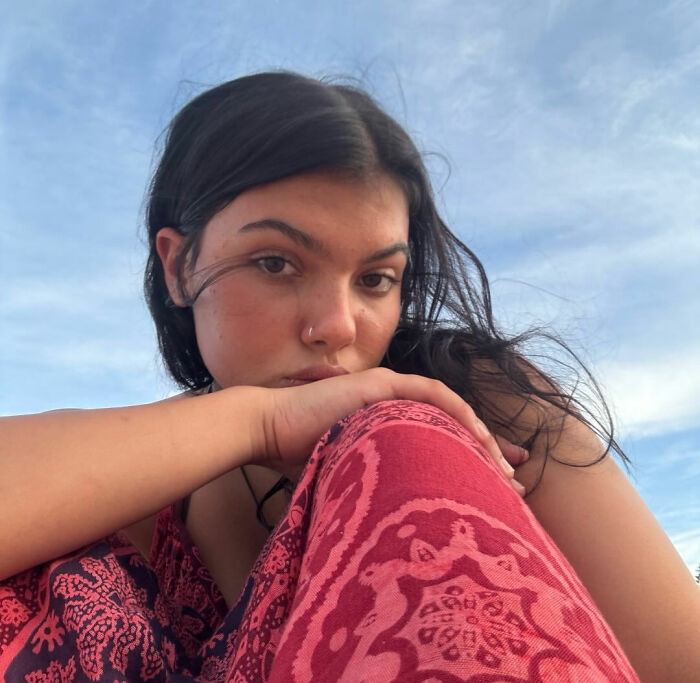 Close-up of a young woman with dark hair and a nose ring wearing a red patterned garment under a blue sky, related to backpacker and dingoes.