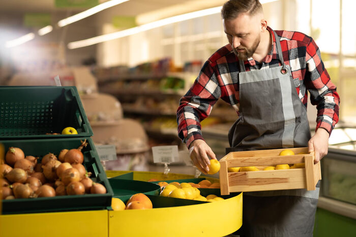 Man in plaid shirt and apron arranging lemons in a box at a grocery store produce section, haunted places concept.