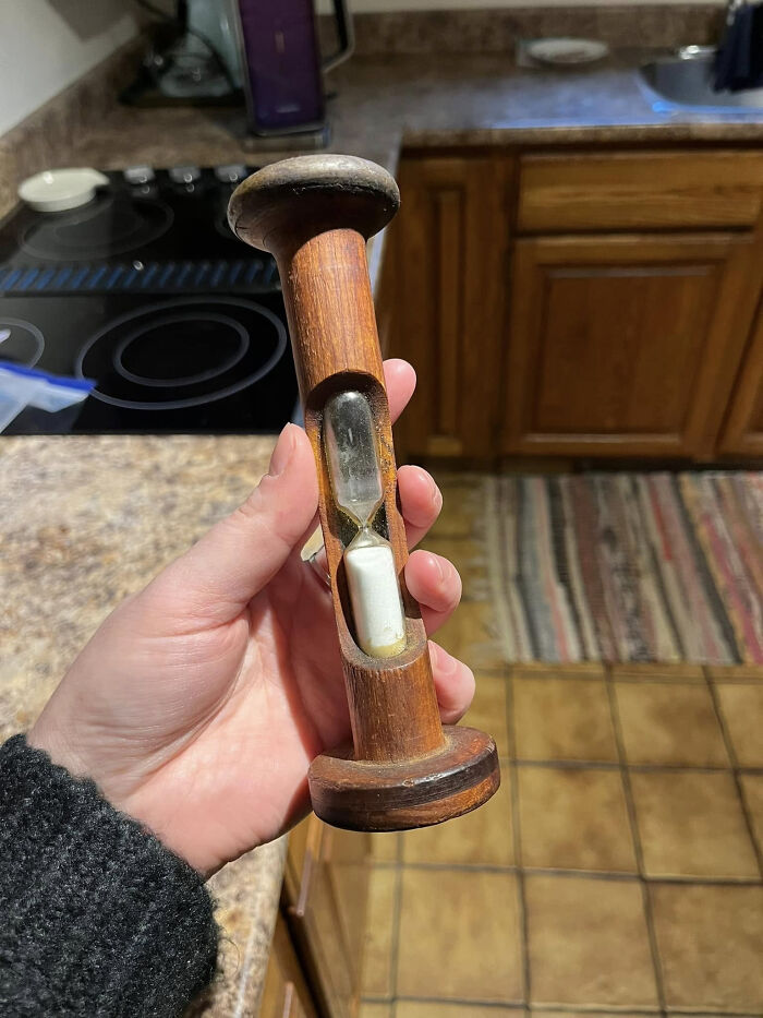 Hand holding a wooden timer with hourglass, one of the unidentified objects the internet solved in a mystery collection.