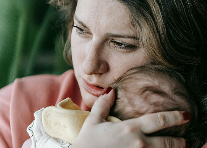 Woman holding baby close, looking concerned and tired while caring for her infant during early morning hours.