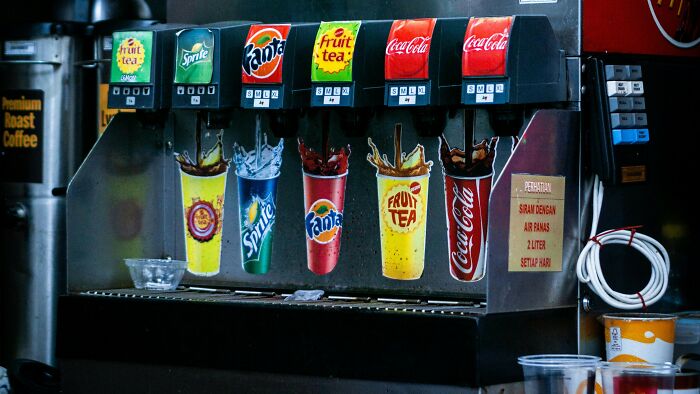 Soda fountain machine pouring various drinks including Sprite, Fanta, Coca-Cola, and fruit tea in a beverage dispenser.