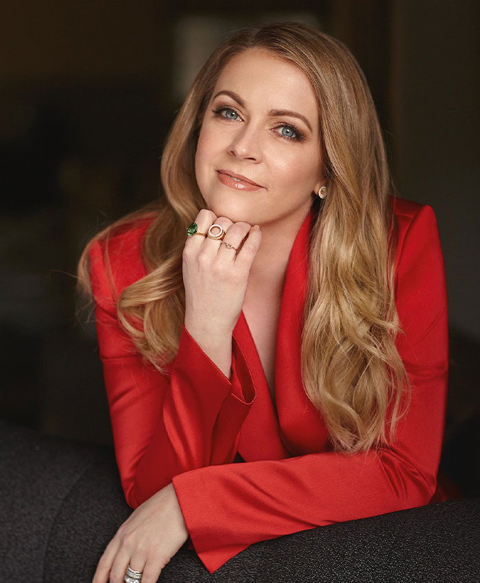 Melissa Joan Hart posing in a red blazer, responding to backlash over Sabrina the Teenage Witch tribute with confidence.