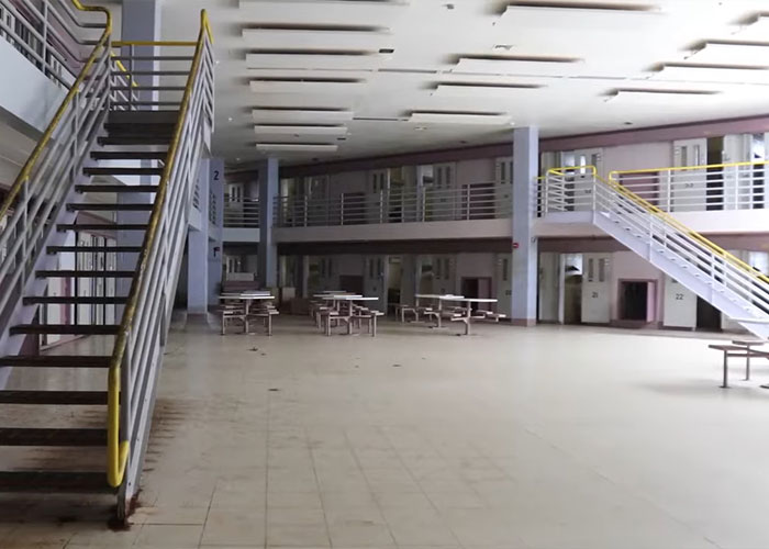 Empty prison common area with tables and staircases, highlighting hygiene issues and prison feuds involving diva alliances.
