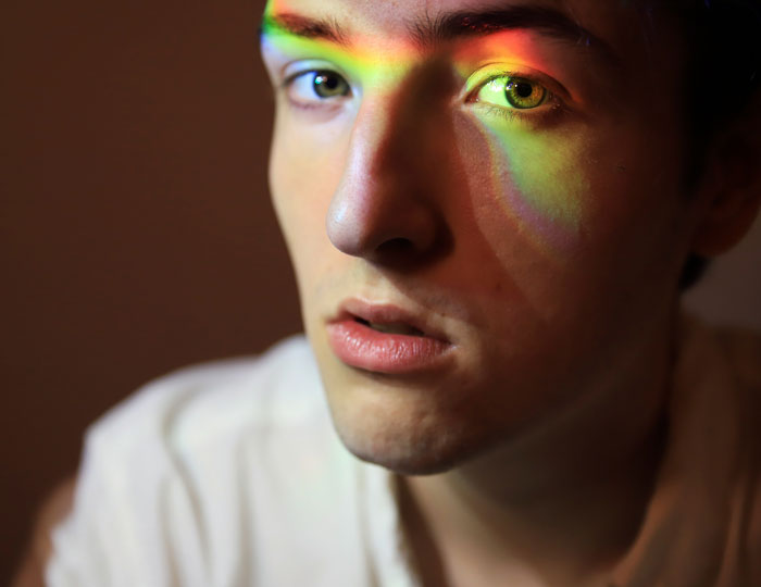 Young man with a serious expression and a rainbow light pattern on his face representing people who lost a friend to a tumour.