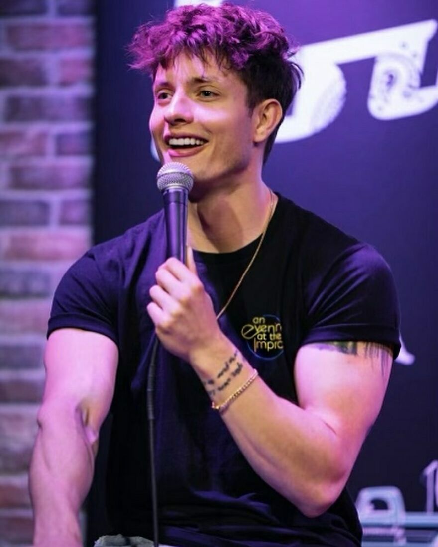 Matt Rife performing stand-up comedy, smiling and holding a microphone on stage with a brick wall background. Matt Rife performing stand-up comedy, smiling and holding a microphone on stage with a brick wall background.