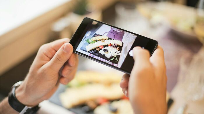 Person taking a photo of food on a smartphone, illustrating peer pressure.