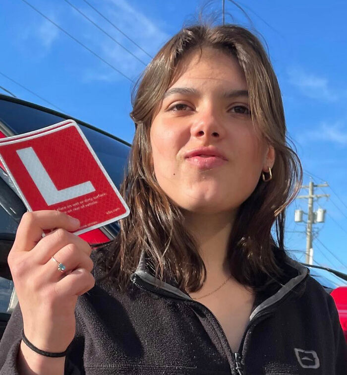 Young woman holding a learner driver sign outdoors with clear sky, related to a backpacker cause of passing and dingoes.