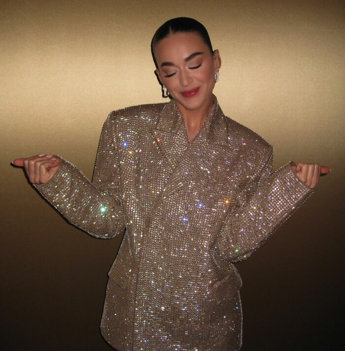 Katy Perry wearing a sparkling jacket with eyes closed and a subtle smile amid controversy over her response to a struggling fan.
