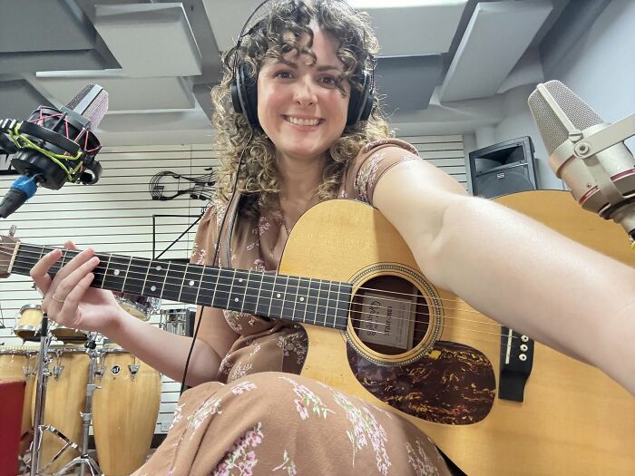 Woman smiling while playing acoustic guitar in a recording studio, showcasing women who chose power tools and lab coats over manicures.