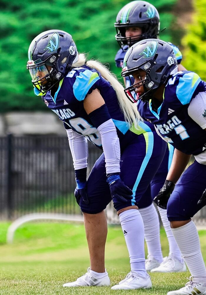 Female athletes in football gear lined up on a field showcasing strength and teamwork with power tools and lab coats spirit.