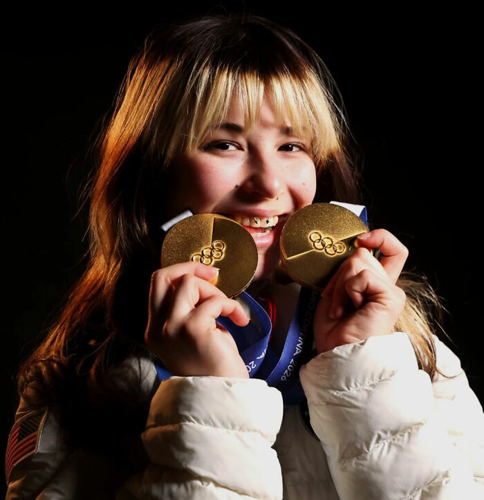 US Olympic hero Alysa Liu smiling and holding two gold medals against a dark background.