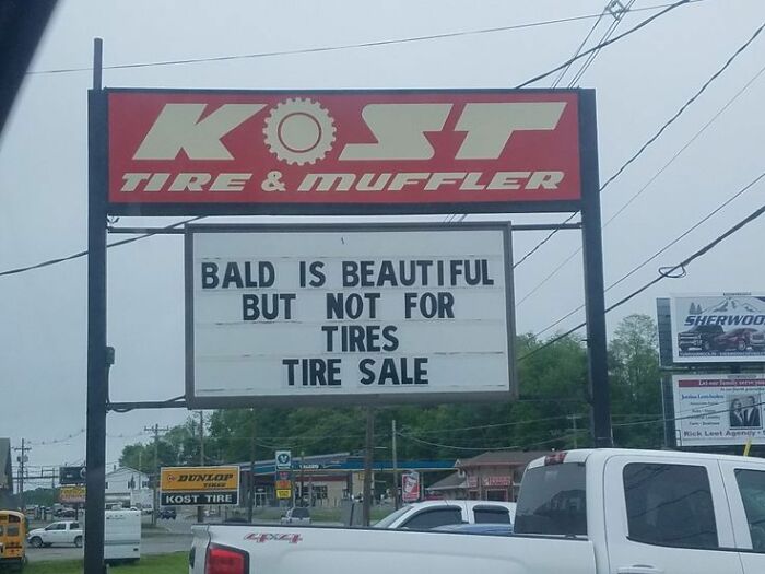 Humorous tire shop sign reading bald is beautiful but not for tires during tire sale at Kost Tire & Muffler.