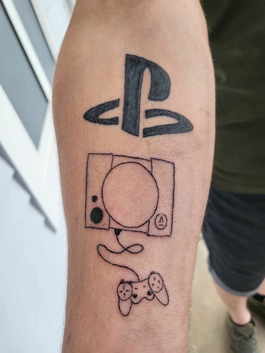 Tattoo featuring a PlayStation logo and a hand-drawn gaming console and controller on a person's forearm.