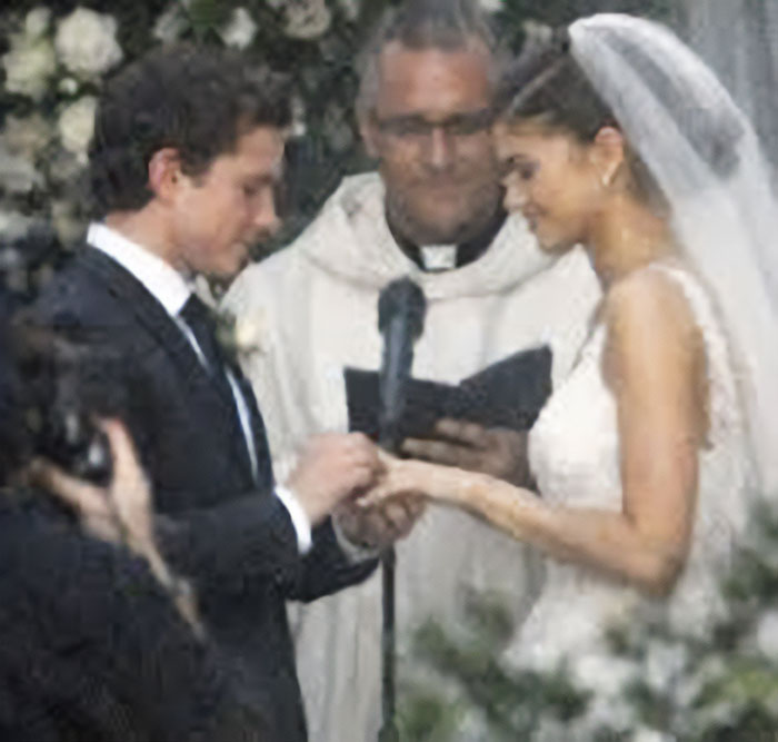 Zendaya and Tom Holland exchanging rings during wedding ceremony with officiant holding a microphone and book nearby