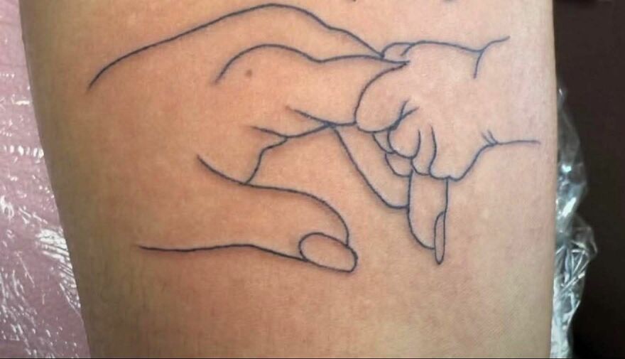 Minimalist tattoo showing an adult hand and a baby hand holding fingers, a unique design raising questions about tattoos.