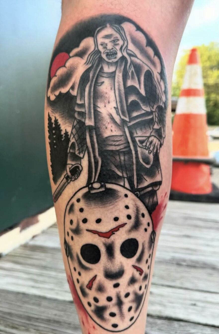 Tattoo of a horror-themed figure holding a weapon above a detailed Jason-style hockey mask on a leg.