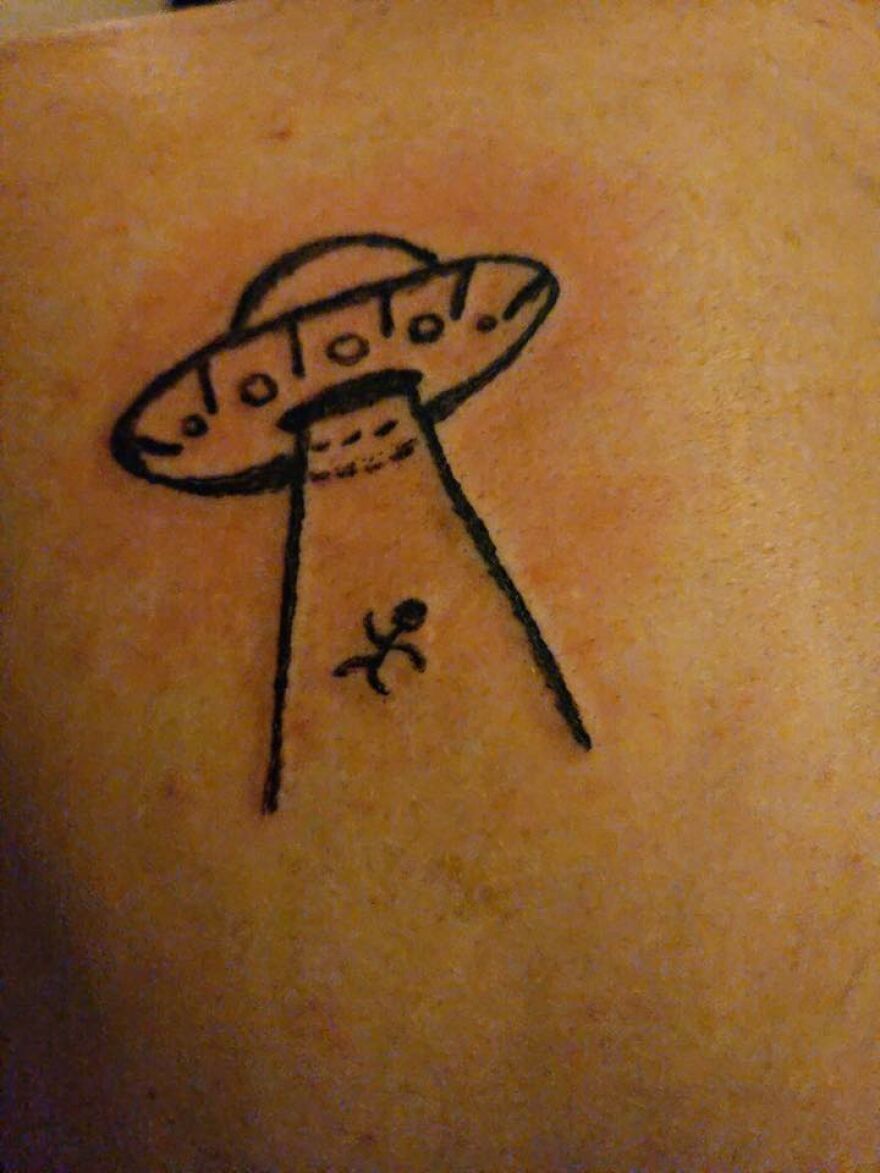 Simple black line tattoo of a UFO abducting a stick figure on skin, an unusual tattoo design making viewers question choices.
