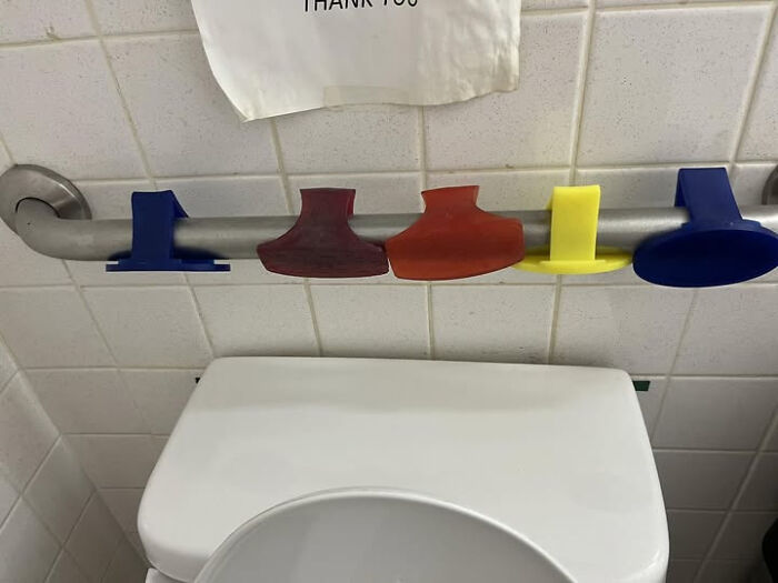 Colorful unidentified objects hung on a bathroom wall grab bar, featuring various shapes and sizes in a tiled restroom.
