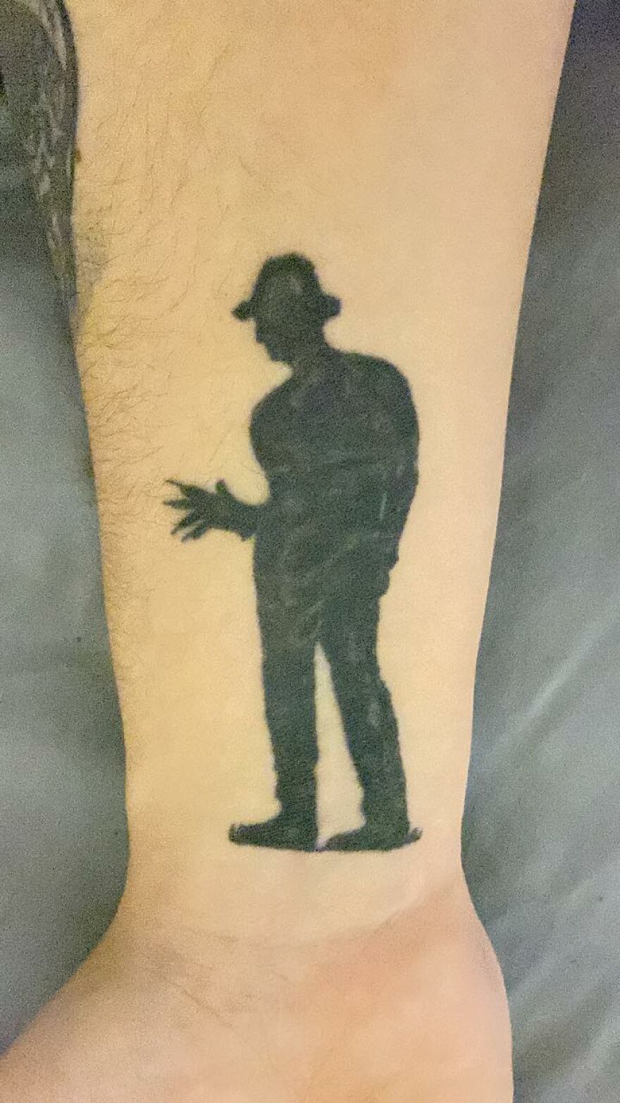 Tattoo of a shadowy figure wearing a hat on a person's forearm, a curious example of unusual tattoos and tattoo artists.