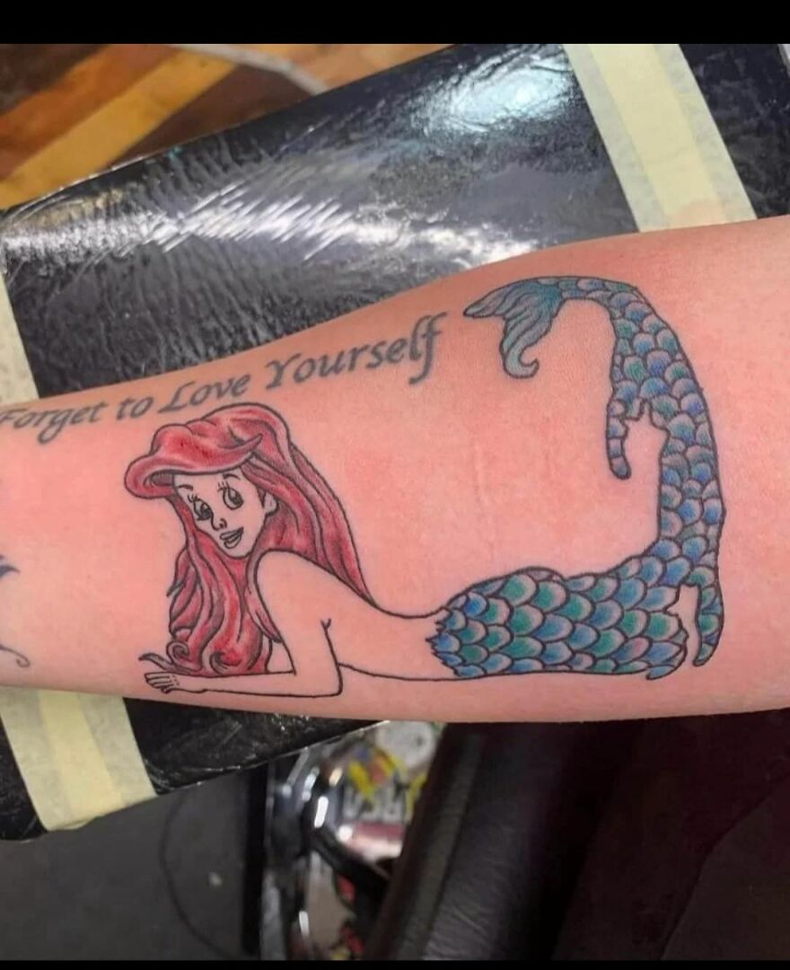 Tattoo of a mermaid with red hair and blue scales on a forearm, showcasing unique and questionable tattoo art styles.