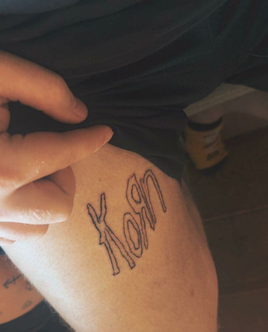 Tattoo of band name Korn on thigh with uneven, shaky lines showing questionable tattoo artistry and choices.