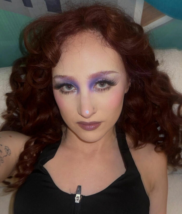 Chappell Roan with red hair and bold purple eye makeup lying down, related to Jude Law's ex and bodyguard dispute.