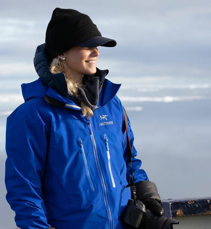 Mulher com jaqueta Arc'teryx azul e chapéu preto segurando uma câmera ao ar livre, relacionada ao suposto tópico da nova namorada de Robert Irwin.