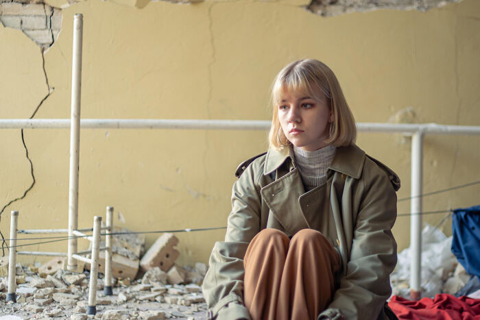 Young woman sitting alone in a worn space, reflecting on tough reasons for staying in a relationship despite hating partner.