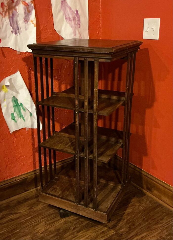 A tall, dark wooden bookshelf, a great thrift store jackpot, standing in a corner with red walls.