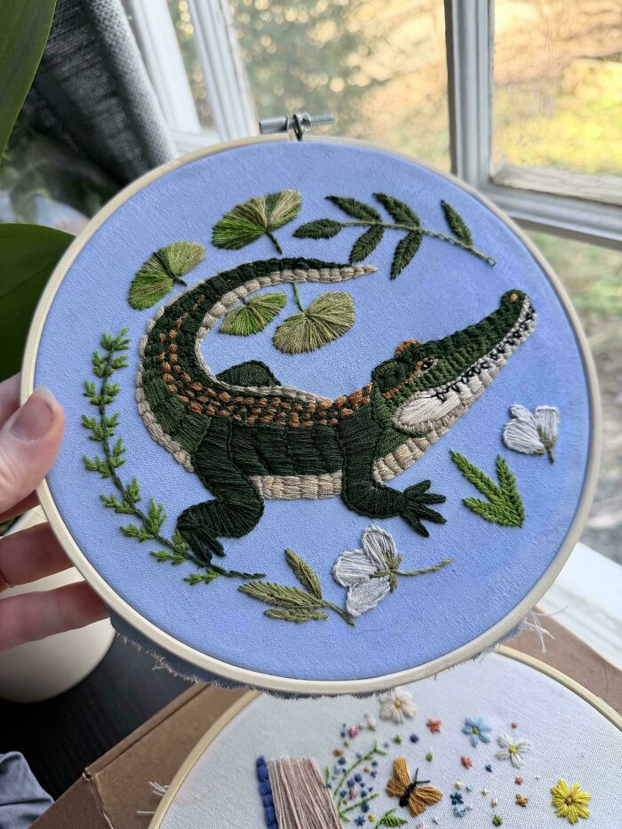 Stunning embroidery creation of an alligator with lily pads and leaves on a blue background, inspiring embroidery hobby.