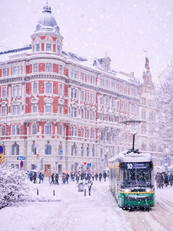 A snow-covered street with a tram and beautiful architecture, featuring a grand red and white building.