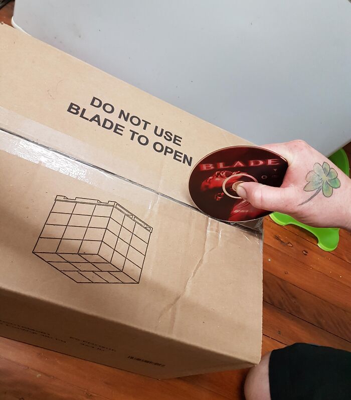 Person using a Blade DVD to open a cardboard box with sarcastic warning not to use a blade to open it.