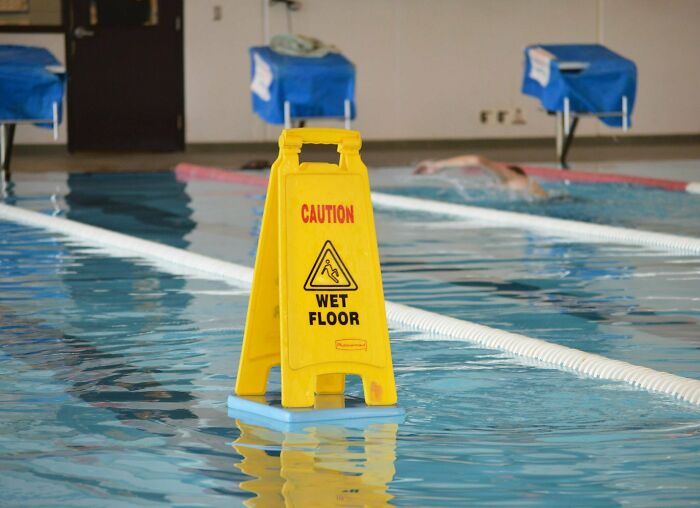 Yellow caution wet floor sign placed in a swimming pool, highlighting sarcastic images for chronic irony humor.