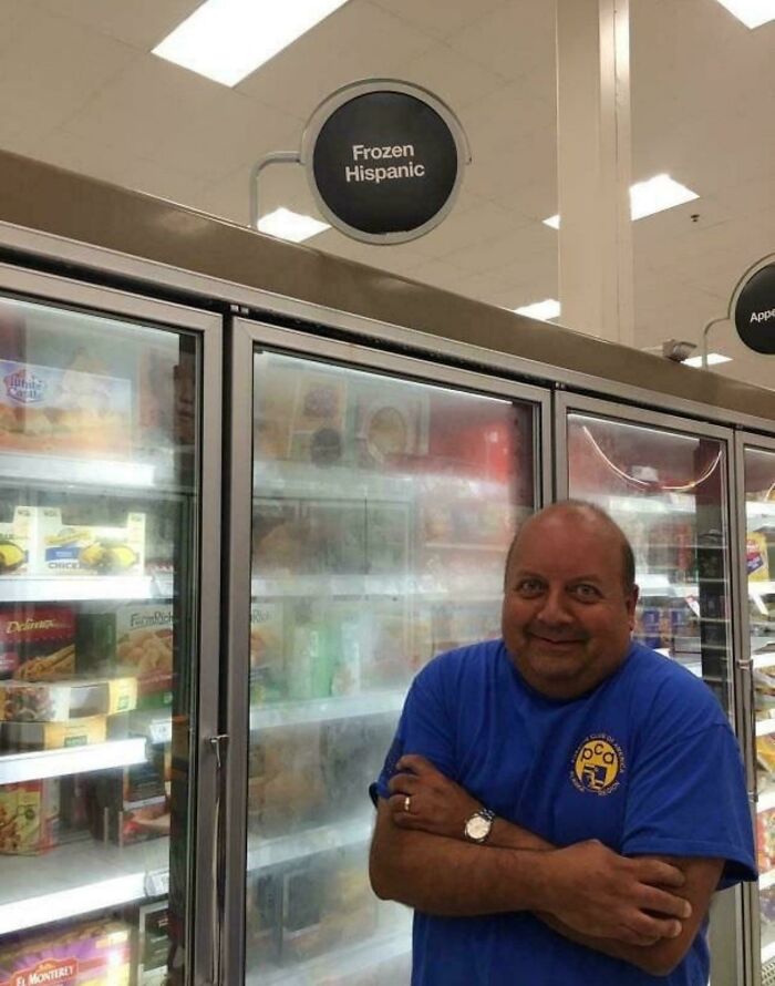 Man standing sarcastically in front of a freezer section labeled Frozen Hispanic, illustrating ironic humor in a grocery store.
