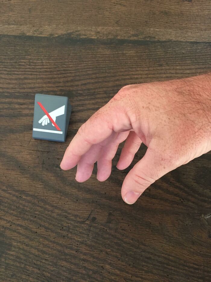 Hand reaching toward a no touching sign on a wooden surface, illustrating sarcastic images and irony concept.