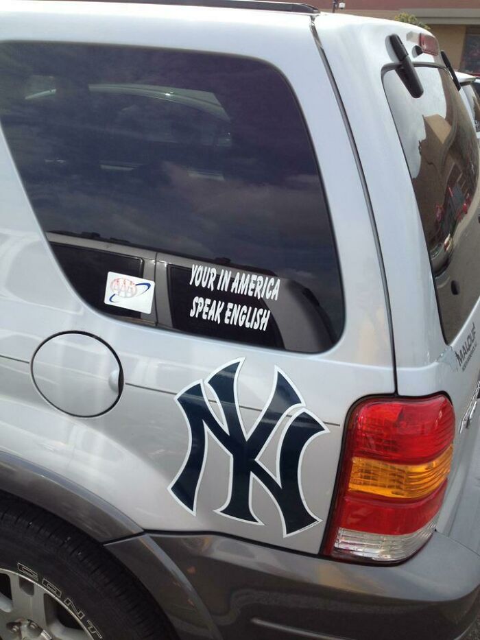 Car window sticker with sarcastic grammar error saying "Your in America speak English" on a silver SUV.
