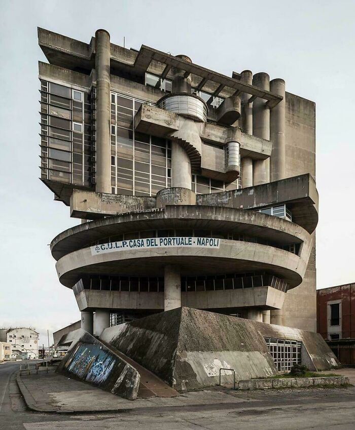 A brutalist building with multiple concrete levels and exposed pipes, resembling a structure for an evil mastermind.