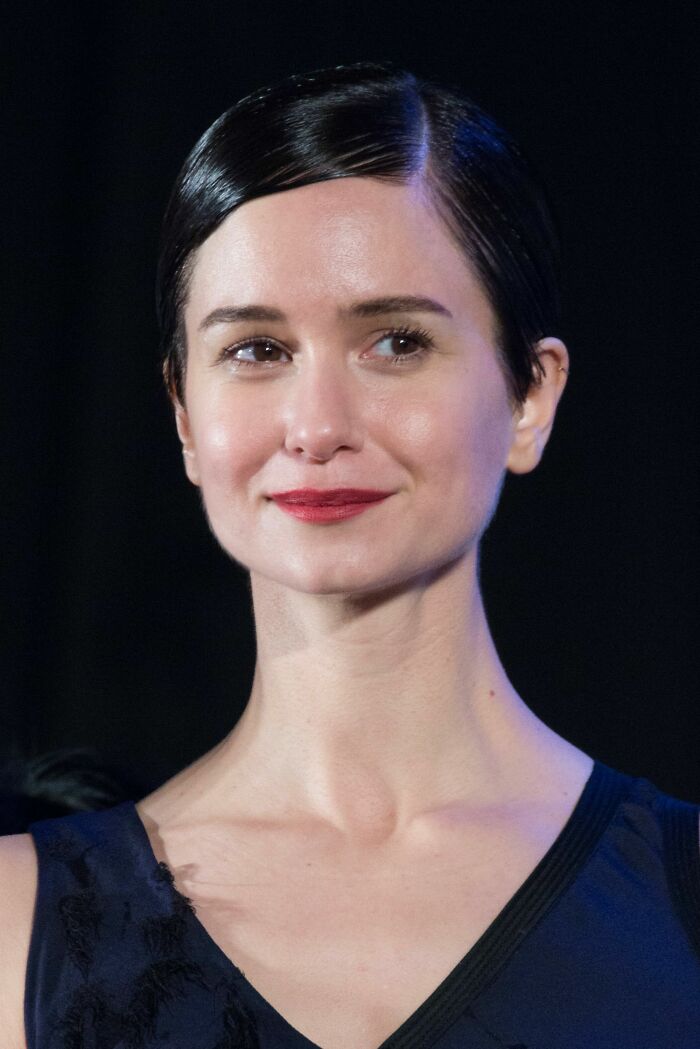 Katherine Waterston with slicked-back hair and red lipstick attending an event highlighting her bio and career.