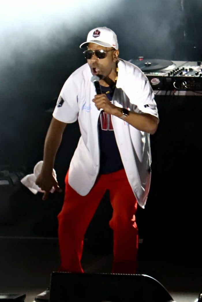 Tone Lōc performing live on stage wearing sunglasses and a white jersey with red pants.